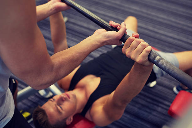 zwei junge männer mit langhantel muskeln zeigen im fitnessraum - spotting stock-fotos und bilder