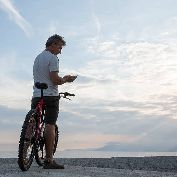 istock Man checks text from bicycle saddle, at beach 483913488
