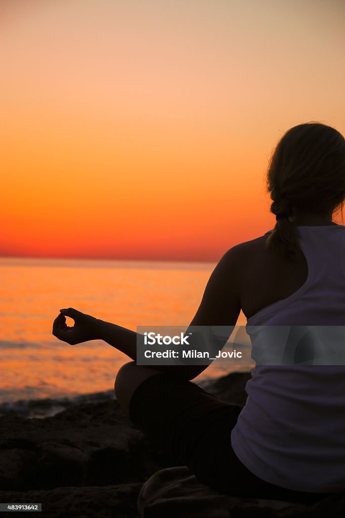 The women in a pose of a lotus The women in a pose of a lotus. A sunset above ocean In Silhouette Stock Photo