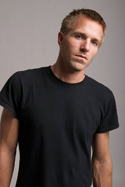 Young Man in Black T-Shirt Looks at Camera Bad Attitude Blond guy stands looking at the camera with a bit of attitude in his black T-shirt  black men with blonde hair stock pictures, royalty-free photos & images