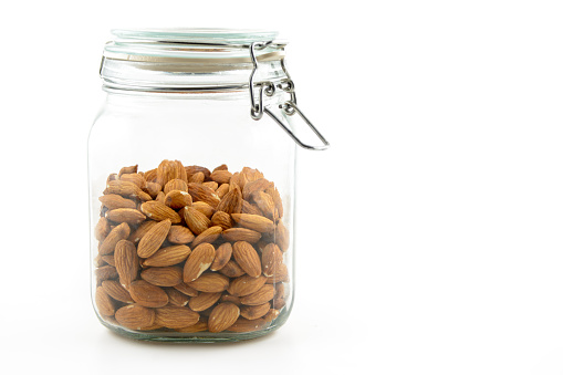 dried whole almonds in a clear glass jar with  a metal clasp and lid on white background