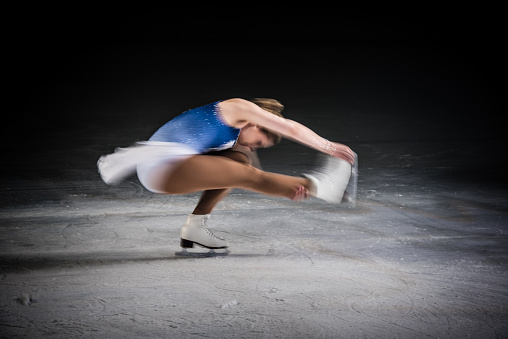 Young female figure skater performing on ice rink, stretching her leg.