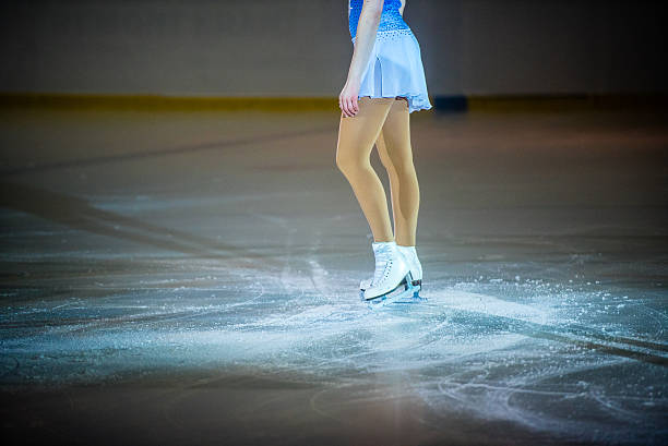 Young female figure skater performing Young female figure skater wearing ice skates standing on ice rink, low section. figure skating stock pictures, royalty-free photos & images