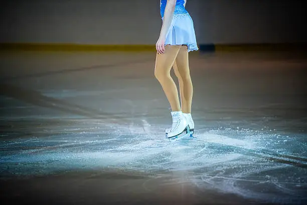 Young female figure skater wearing ice skates standing on ice rink, low section.