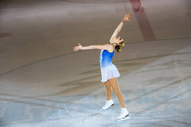 Young female figure skater performing on ice rink, looking up.