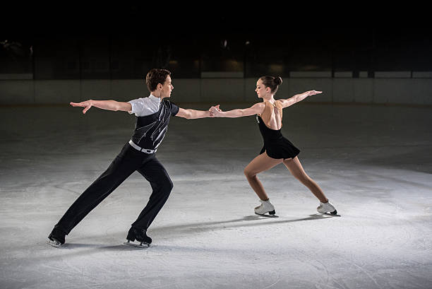 Young figure skating pair performing Man and woman figure skaters performing on ice rink, both holding hands eachother with arm outstretched. figure skating stock pictures, royalty-free photos & images