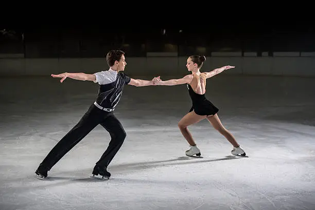 Man and woman figure skaters performing on ice rink, both holding hands eachother with arm outstretched.