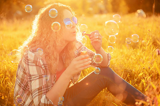 young girl with long hair blowing a bubble wand in clear blue sky sunset