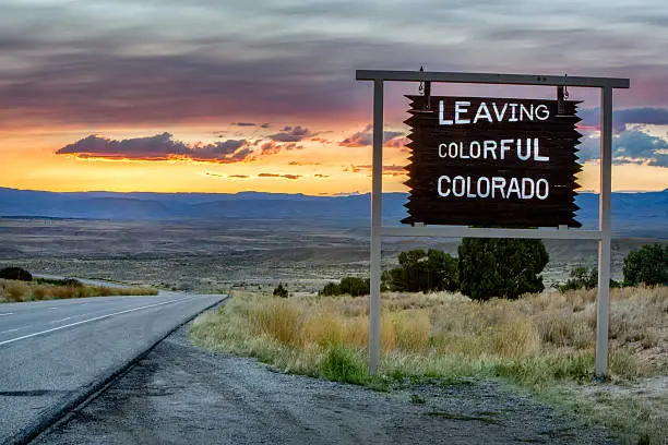 Beautiful sunset behind a vanishing roadway with a sign that says leaving colorful Colorado.