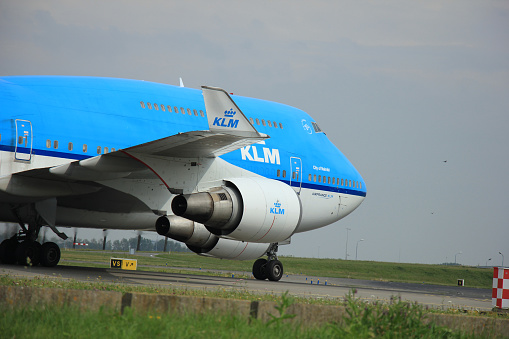 Close Up View Of KLM Passenger Airplane Tail Parked At Schiphol International Airport Amsterdam The Netherlands Europe.Including Architecture And Buildings,Land Vehicle,Passengers Loads On The Ground