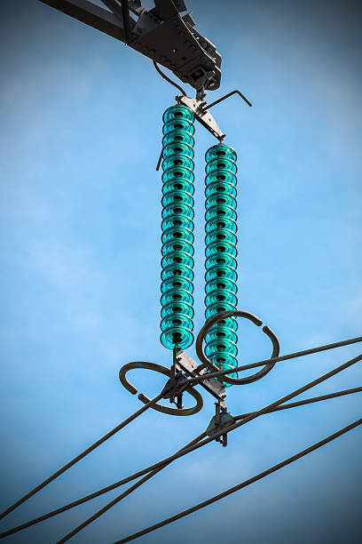 Vertical composition photography shot without people, of close-up of glass insulator circles from high voltage metallic electricity pylon with power line cable. This image was taken against blue sky, with a small vignetting effect.