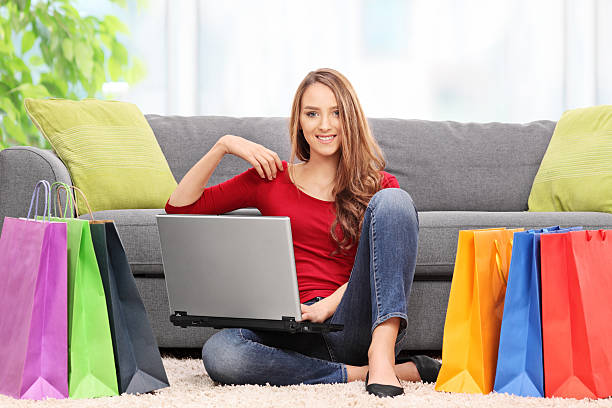 jeune femme tenant un ordinateur portable et un salon - women holding shopping bag living room photos et images de collection