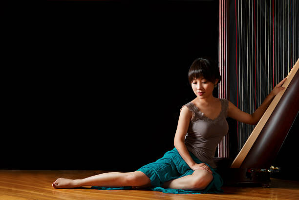 A female musician sitting on the ground with her harp and look on the ground.