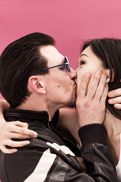 A young man and woman posing in vintage casual clothing, blowing air kisses, expressing joy and affection against a vibrant blue background. Ideal for concepts of fun, love, or lifestyle.