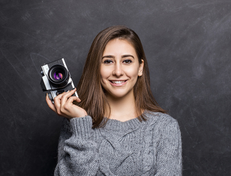 Young beautiful woman holding a vintage SLR film camera over black background, studio shot