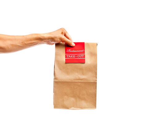 A takeout deliveryman delivering convenience fast food package paper bag container to customers. Isolated and cut out on white background. Hand holding a brown bag of take out food with a red restaurant label. Photographed close-up in studio.