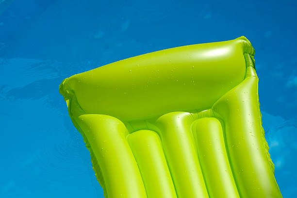 green air mattress is floating in blue water of a swimming pool. inflatable  is only partly shown