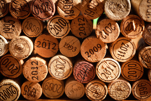 A large group of used wine cork stopper with various vintage years showing forming the background with a rustic wood surface in the foreground. Background design for the wine industry, wine tasting events, and restaurants and bars businesses. Photographed with copy space. Studio still life close-up photography in horizontal format.