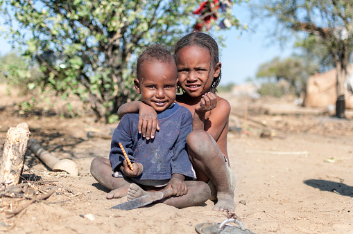 Portrait of two hungry african children who are growing up in poverty and miserable surroundings. The small boy is happy, he holding a cookie. Both children looking at camera. The climate is arid and tropical.
