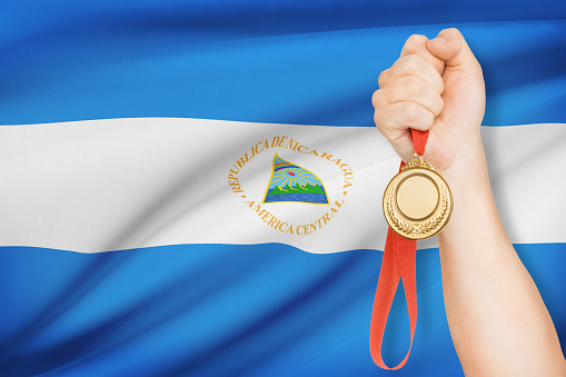 Sportsman holding gold medal with flag on background - Republic of Nicaragua