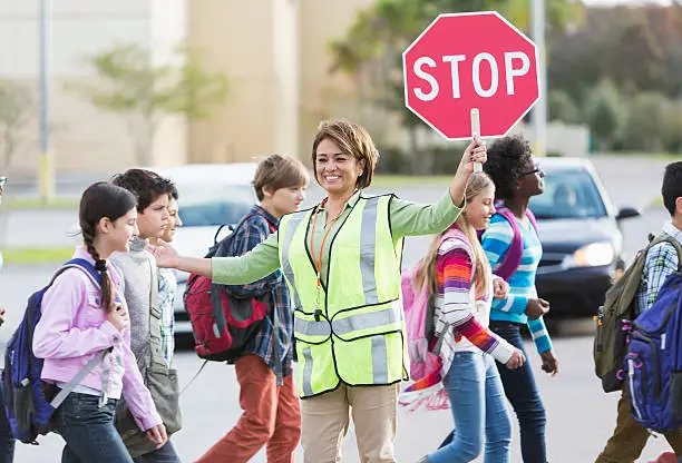 School crossing guard (Hispanic mature woman, 50s) helping children walk across street.  Focus on woman.