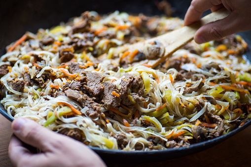 Hands holding wok with traditional asian  noodles with meat and vegetables.