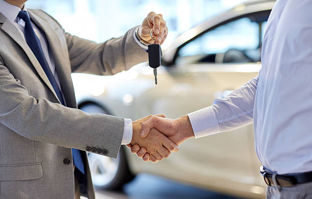 close up of handshake in auto show or salon auto business, car sale, deal, gesture and people concept - close up of dealer giving key to new owner and shaking hands in auto show or salon car key photos stock pictures, royalty-free photos & images
