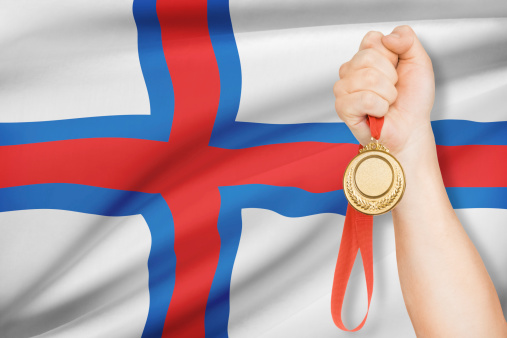 Sportsman holding gold medal with flag on background - Faroe Islands