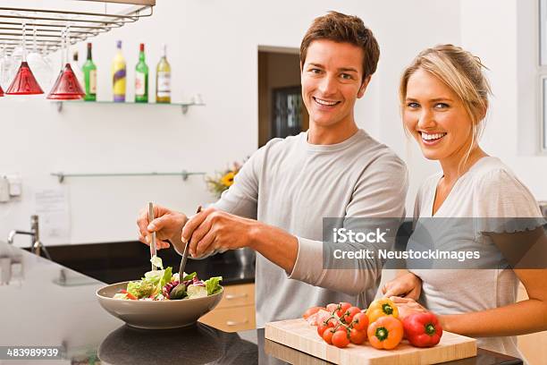 Young Man Tossing Salad And Woman Cutting Vegetable Stock Photo - Download Image Now