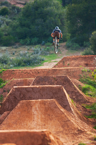 A male mountain biker rides a set of jumps at a dirt jump park.