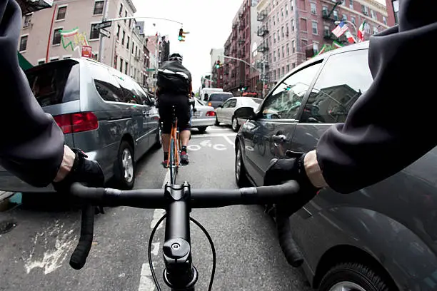 The handlebar view of a male bike courier in New York City going past cars on both sides in a traffic jam during rush hour. 