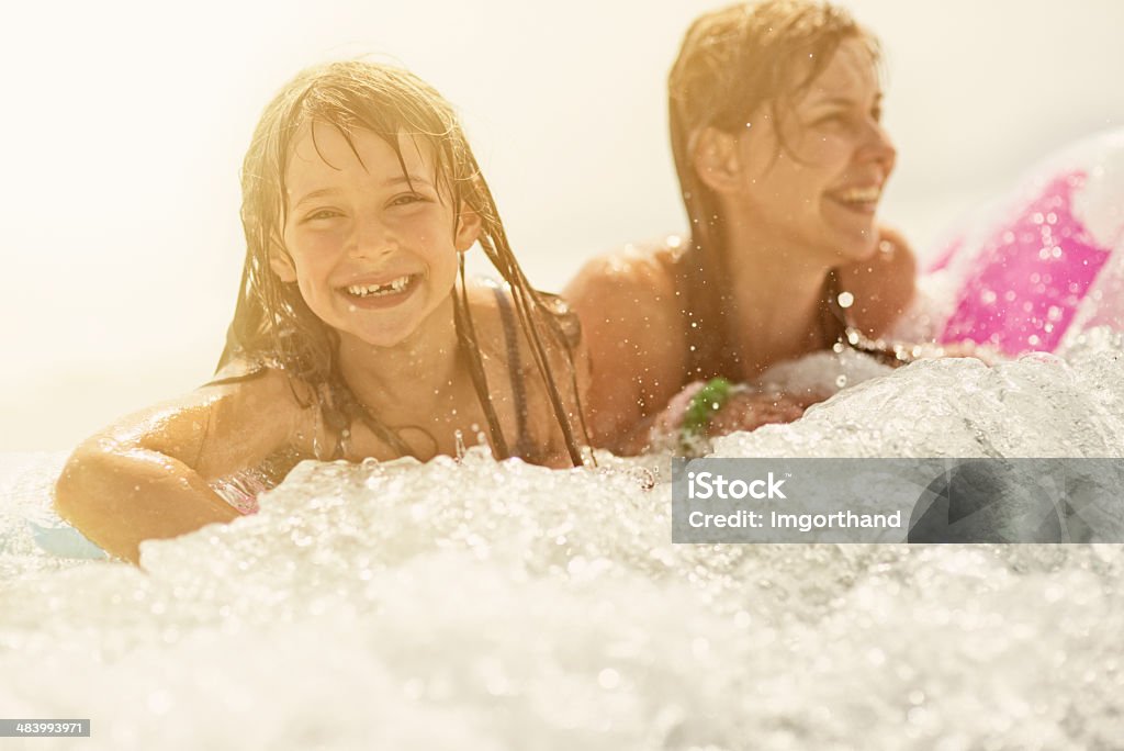 Daughter and mother having fun in sea Little girl and mother with inflateable raft being splashed by waves in sea. 6-7 Years Stock Photo