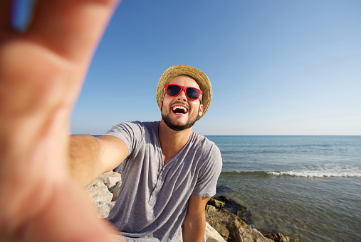 Happy man on vacation laughing at the beach taking selfie