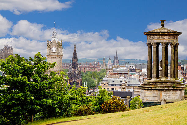 Edinburgh Skyline with Historic Buildings, Scotland, United Kingdom. The image is taken from Calton Hill and shows Scott Monument, Edinburgh Castle (far left) and the Dugald Stewart Monument in the foreground. The Pinces Street is seen down below. Scottish flag is flying atop the building. Canon EF 70-200 mm f/4L lens. Deep blue sky with clouds is in background. HDR photorealistic image.