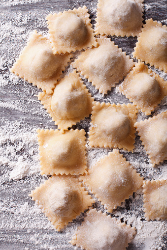 Italian uncooked ravioli with flour on the table closeup. vertical view from above