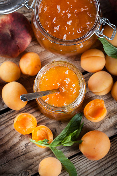 Apricot jam on wooden board - apricots, peaches and mint leaves in the background