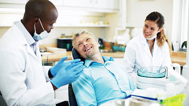 zahnarzt gespräch mit patienten, die lächeln zurück als assistant uhren - dentist dentist office patient discussion stock-fotos und bilder