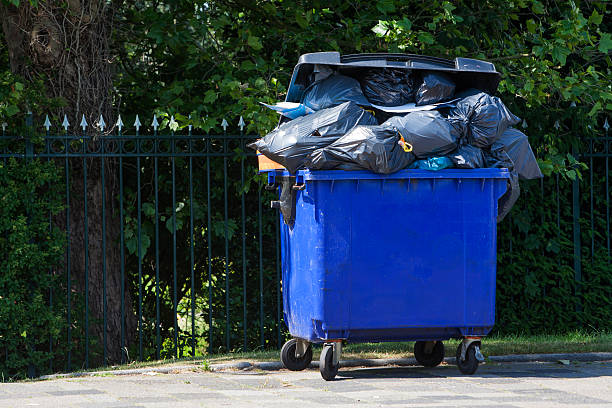 Blue wheeled garbage can Blue wheeled garbage can overflowed with garbage bags in the street, in front of a garden fence. overflowing dumpster stock pictures, royalty-free photos & images