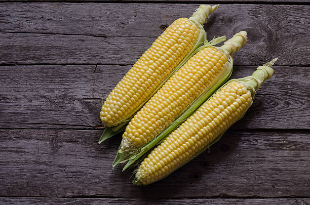 istock corn cob and green leaves on wooden background 484006434