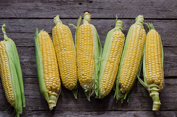 istock corn cob and green leaves on wooden background 484006446