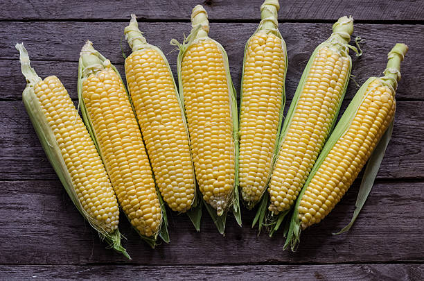 istock corn cob and green leaves on wooden background 484006452
