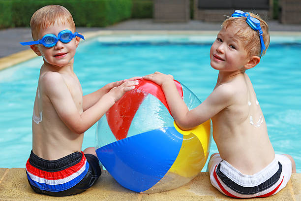 deux garçons jouant avec un ballon de plage coloré sur la piscine - beach ball swimming pool ball child photos et images de collection