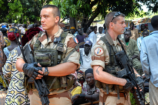 Moundou, Chad - October 30, 2012: The photo speak about two French army soldiers who are guarding poor village in Africa. They are protecting place full of innocent african people. Soldiers wearing military french uniform, holding guns, controlling and keeping the area safe. 