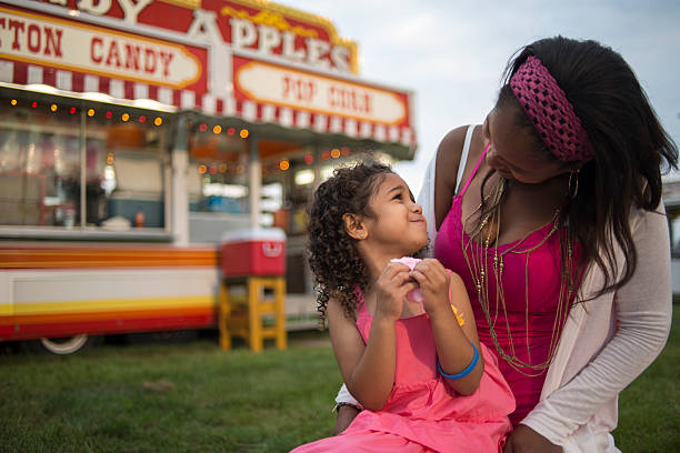 Eating Cotten Candy Child sitting on mother's lap eating cotton candy. Fair food vendor in background. agricultural fair stock pictures, royalty-free photos & images