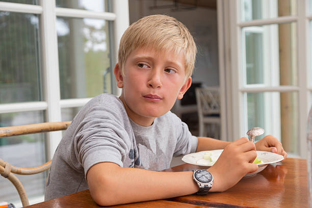 istock Young blond boy with plate of yogurt outside looking sideways. 484012762