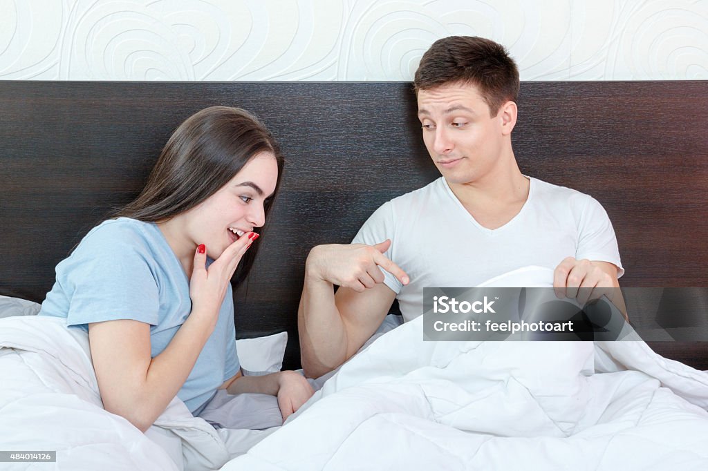 Sexy young couple in morning, domestic atmosphere Handsome satisfied man sure in himself showing under cover in bedroom strong penis erection to pretty surprised woman. Sexy young couple in morning, domestic atmosphere. Photo of healthy male potency. 2015 Stock Photo