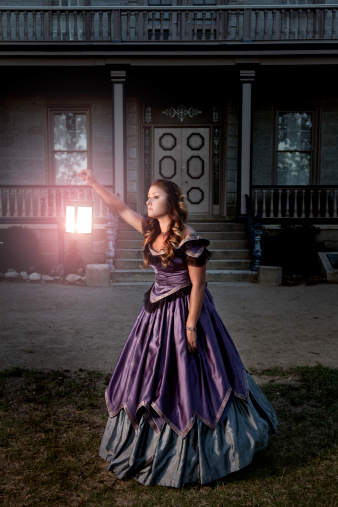 A young victorian woman searching outside her home with an illuminated lantern.