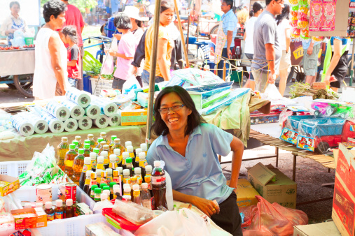 Noen Maprang, Thailand - May, 24th 2013: Laughing female vendor sitting at her marketstand on market in small town in province of Phitsanulok. In background are walking and are shopping Thai people.