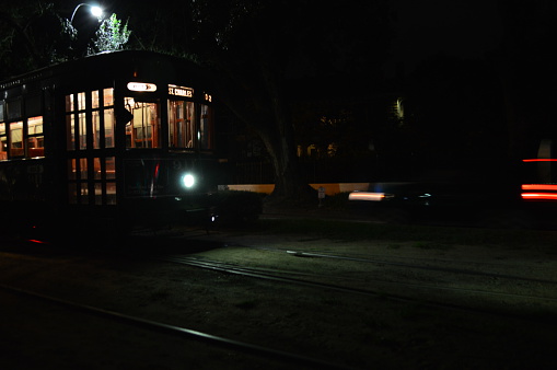 Night time view of a street car on St. Charles Avenue in New Orleans, Louisiana.  On the right side of the photo are streaking lights from a moving vehicle going down the street next to the streetcar.