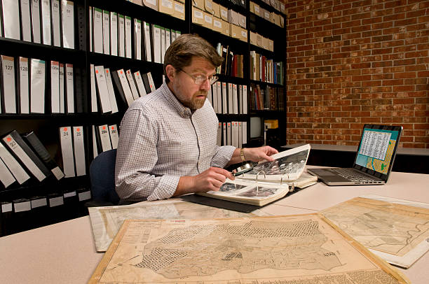 Researcher in archive, searching through maps and photographs. 